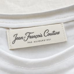 Eticheta țesută Jean-François Couture — cusută à la main în gulerul tricoului alb